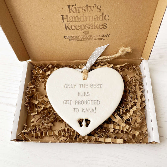 Pearlised white clay hanging heart with baby feet cut out of the bottom and grey personalisation, the heart is personalised with ONLY THE BEST MUMS GET PROMOTED TO NANA!