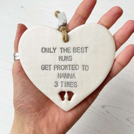 Pearlised white clay hanging heart pregnancy reveal with baby feet cut out of the bottom and grey personalisation, the heart is personalised with ONLY THE BEST MUMS GET PROMOTED TO NANNA 3 TIMES