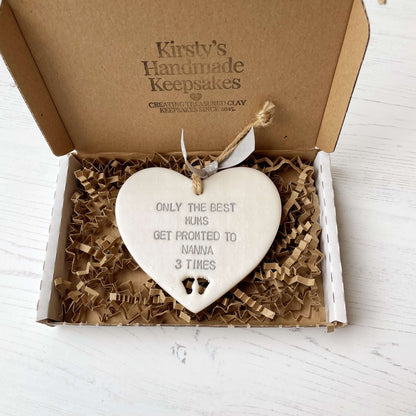 Pearlised white clay hanging heart pregnancy reveal with baby feet cut out of the bottom and grey personalisation, the heart is personalised with ONLY THE BEST MUMS GET PROMOTED TO NANNA 3 TIMES