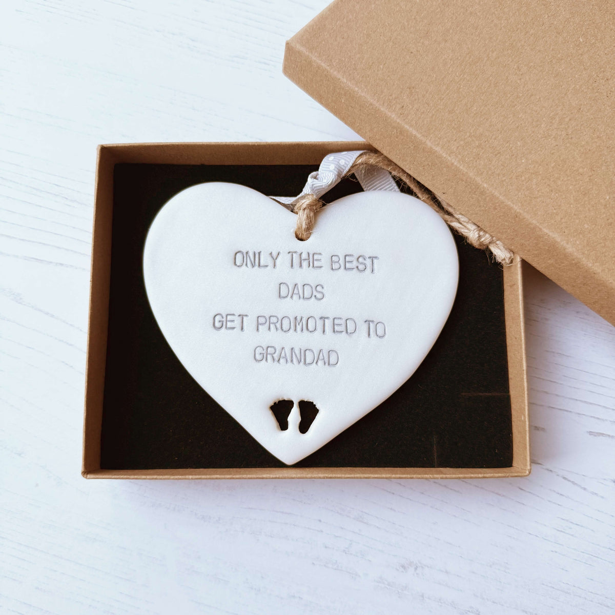 Pearlised white clay hanging heart with baby feet cut out of the bottom and grey personalisation, the heart is personalised with ONLY THE BEST DADS GET PROMOTED TO GRANDAD