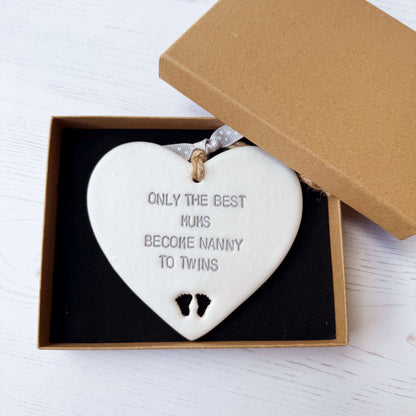 Pearlised white clay hanging heart with baby feet cut out of the bottom and grey personalisation, the heart is personalised with ONLY THE BEST MUMS BECOME NANNY TO TWINS