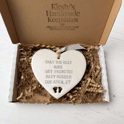 Pearlised white clay hanging heart with baby feet cut out of the bottom and grey personalisation, the heart is personalised with ONLY THE BEST MUMS GET PROMOTED BABY ROSSER DUE APRIL 27