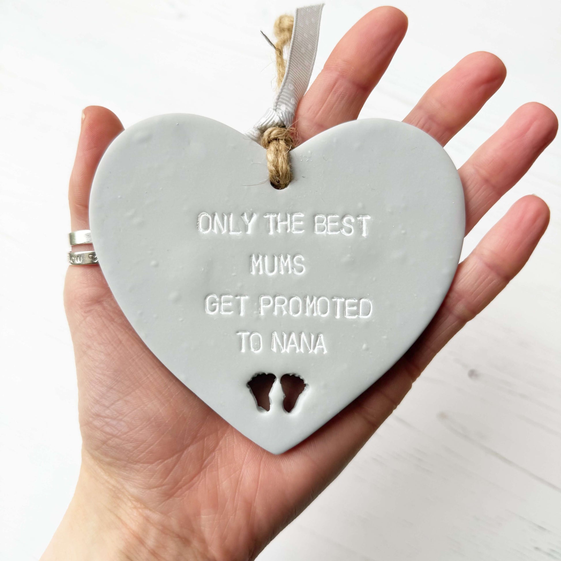 Grey clay hanging heart with baby feet cut out of the bottom and white personalisation, the heart is personalised with ONLY THE BEST MUMS GET PROMOTED TO NANA