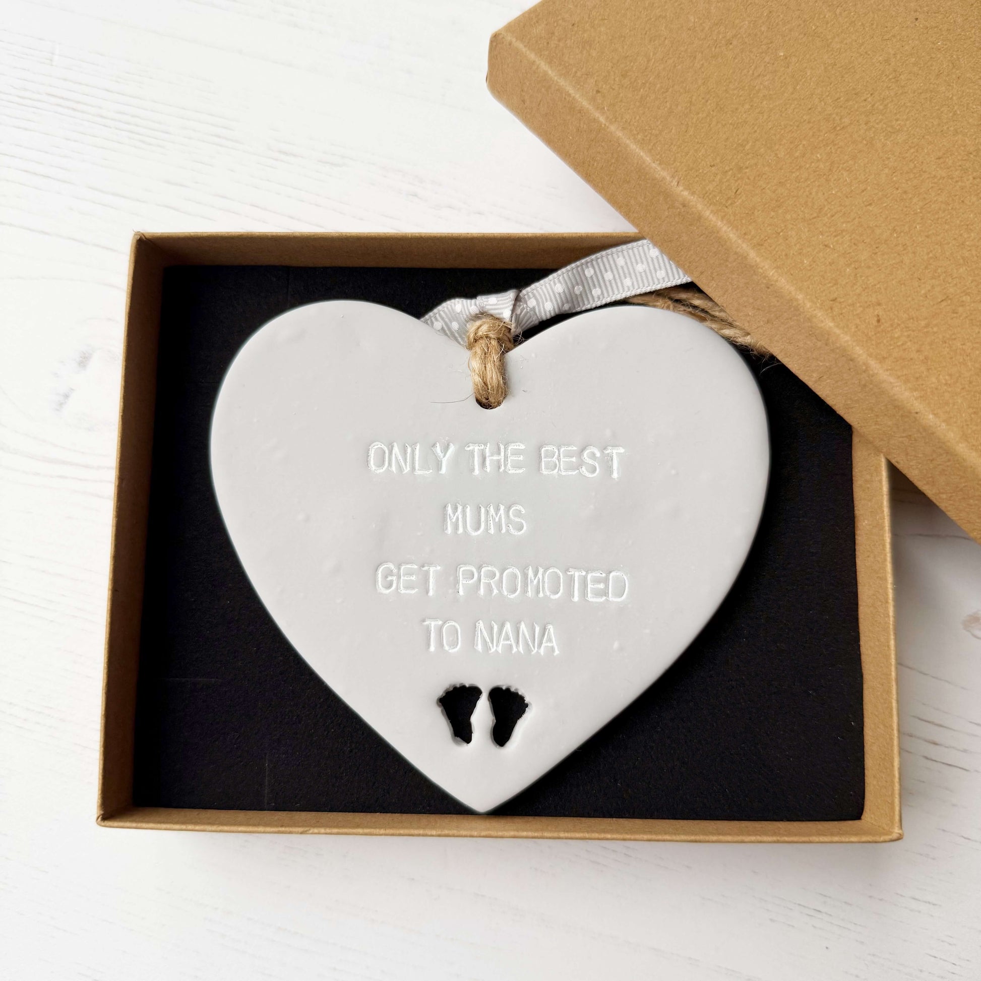Grey clay hanging heart with baby feet cut out of the bottom and white personalisation, the heart is personalised with ONLY THE BEST MUMS GET PROMOTED TO NANA