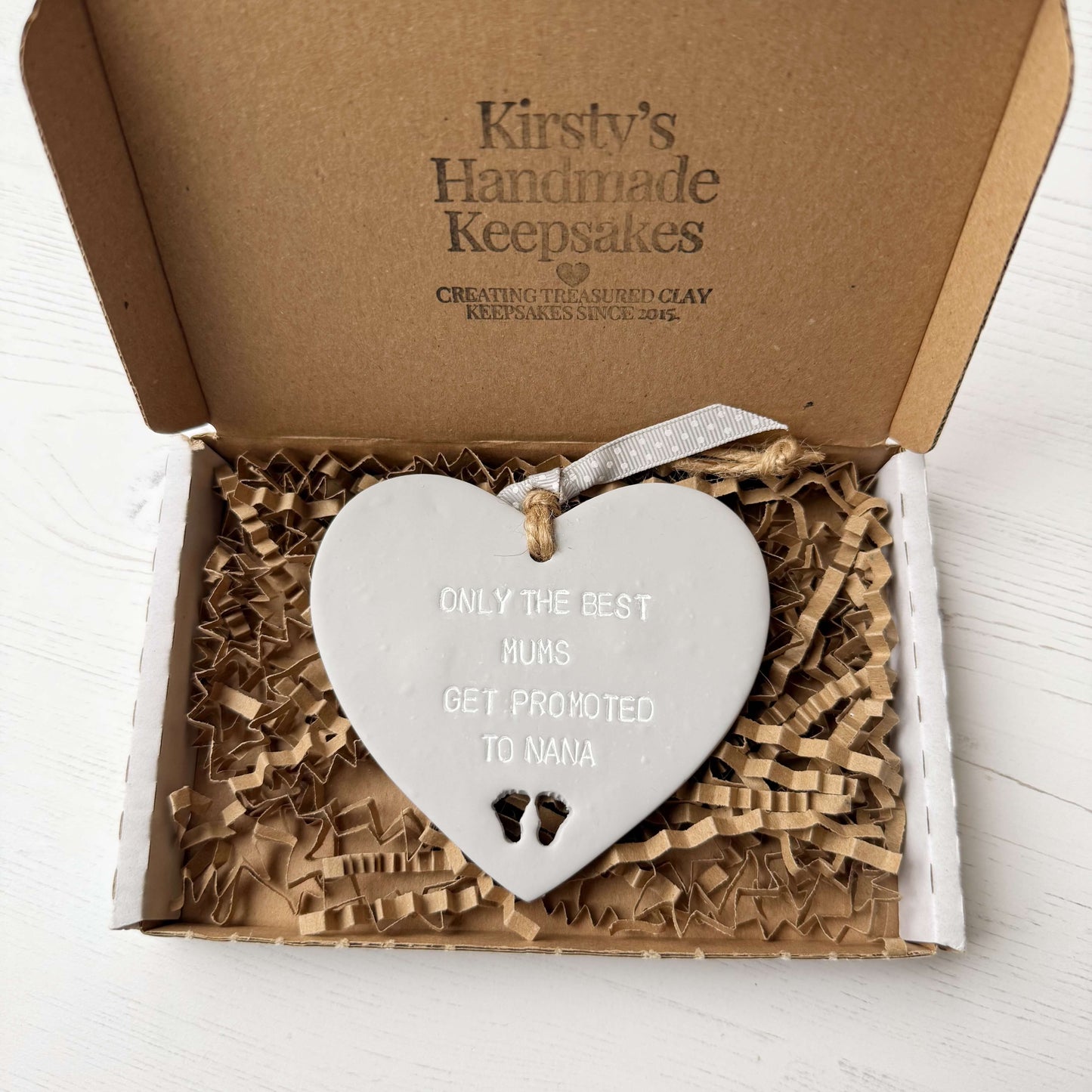 Grey clay hanging heart with baby feet cut out of the bottom and white personalisation, the heart is personalised with ONLY THE BEST MUMS GET PROMOTED TO NANA