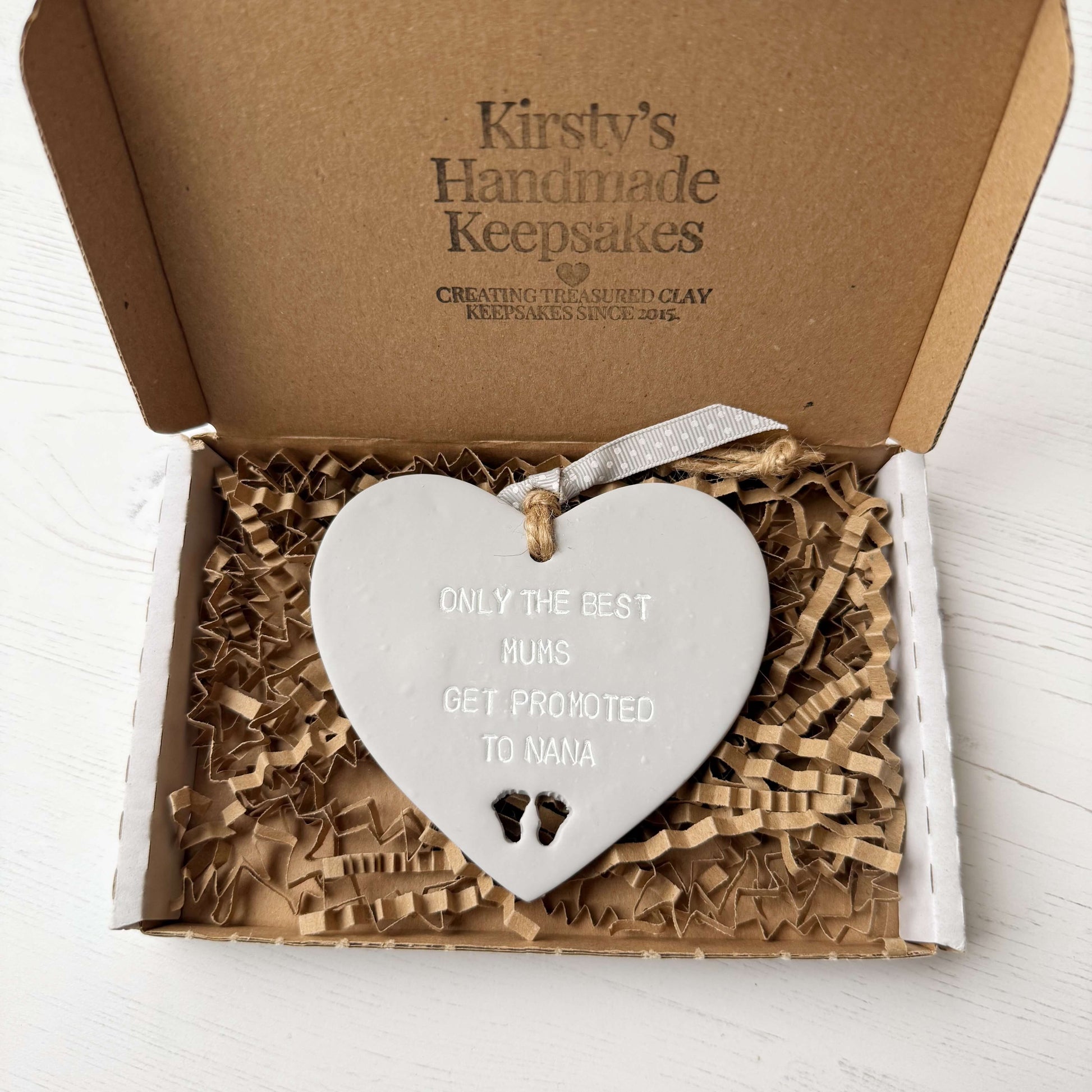 Grey clay hanging heart with baby feet cut out of the bottom and white personalisation, the heart is personalised with ONLY THE BEST MUMS GET PROMOTED TO NANA