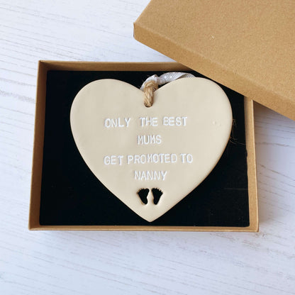 Beige clay hanging heart with baby feet cut out of the bottom and white personalisation, the heart is personalised with ONLY THE BEST MUMS GET PROMOTED TO NANNY