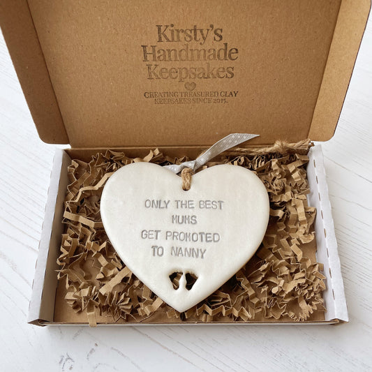 Pearlised white clay hanging heart with baby feet cut out of the bottom and grey personalisation, the heart is personalised with ONLY THE BEST MUMS GET PROMOTED TO NANNY