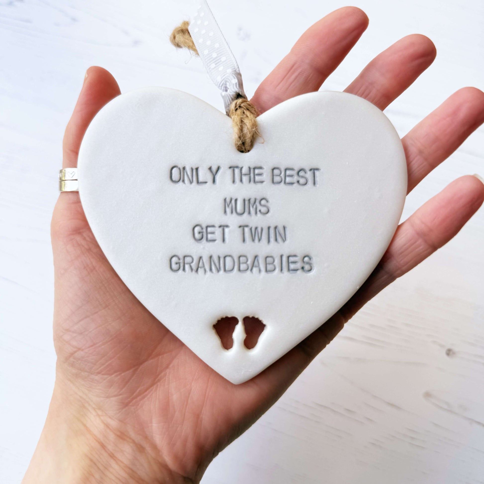 Pearlised white clay hanging heart with baby feet cut out of the bottom and grey personalisation, the heart is personalised with ONLY THE BEST MUMS GET TWIN GRANDBABIES