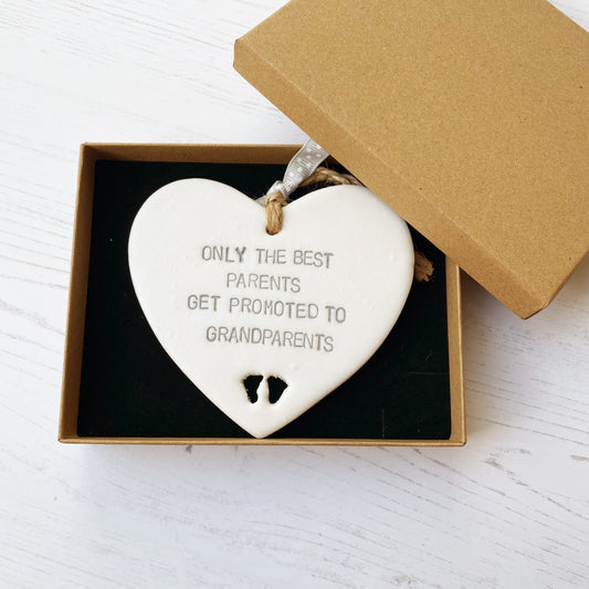 Pearlised white clay hanging heart with baby feet cut out of the bottom and grey personalisation, the heart is personalised with ONLY THE BEST PARENTS GET PROMOTED TO GRANDPARENTS