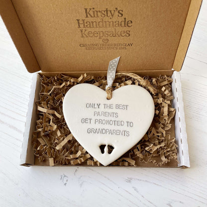 Pearlised white clay hanging heart with baby feet cut out of the bottom and grey personalisation, the heart is personalised with ONLY THE BEST PARENTS GET PROMOTED TO GRANDPARENTS