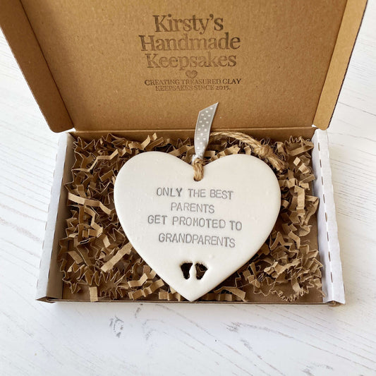 Pearlised white clay hanging heart with baby feet cut out of the bottom and grey personalisation, the heart is personalised with ONLY THE BEST PARENTS GET PROMOTED TO GRANDPARENTS