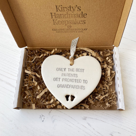 Pearlised white clay hanging heart with baby feet cut out of the bottom and grey personalisation, the heart is personalised with ONLY THE BEST PARENTS GET PROMOTED TO GRANDPARENTS