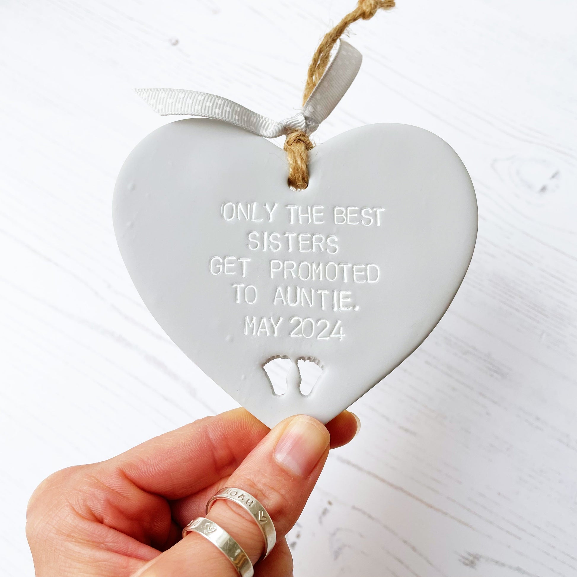 Grey clay hanging heart with baby feet cut out of the bottom, the heart is personalised with ONLY THE BEST SISTERS GET PROMOTED TO AUNTIE. MAY 2024