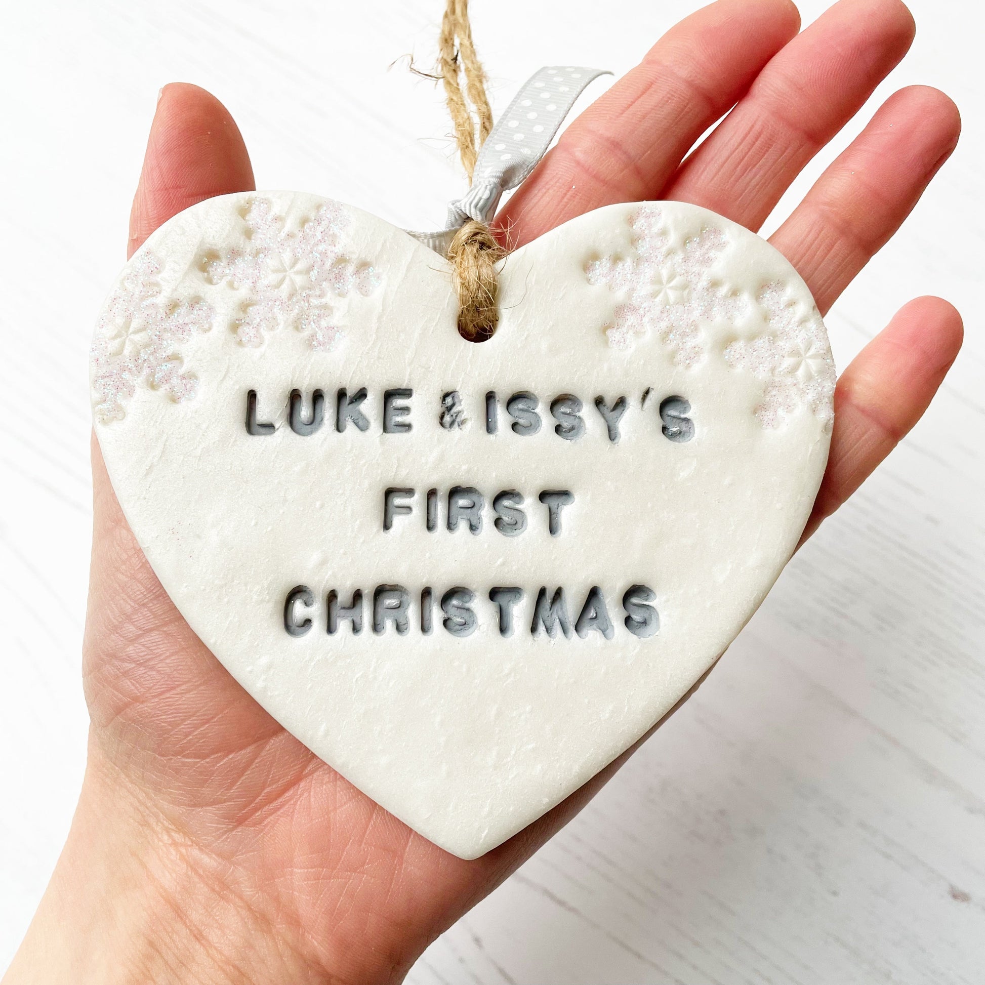 Personalised our first Christmas together heart ornament, pearlised white clay with LUKE & ISSY'S FIRST CHRISTMAS 2020 painted grey, decorated with 2 iridescent glitter snowflakes on either side of the top of the heart