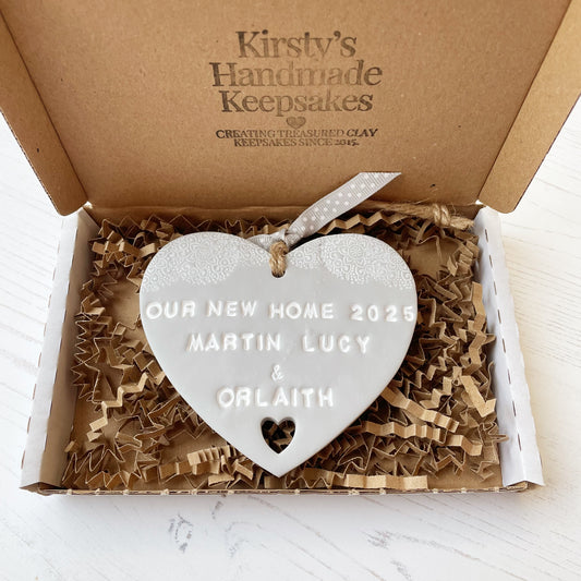 Personalised new home gift grey clay heart with a white lace edge at the top & a heart cut out at the bottom with twine for hanging personalised with OUR NEW HOME 2025 MARTIN LUCY &  ORLAITH