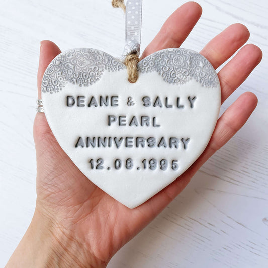 Personalised 30th Pearl anniversary gift, pearlised white clay hanging heart with a grey lace edge at the top of the heart, the heart is personalised with DEAN & SALLY PEARL ANNIVERSARY 12.08.1995