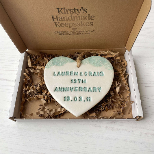 Personalised 13th wedding anniversary gift, pearlised white clay hanging heart with a sage green lace edge at the top of the heart, the heart is personalised with LAUREN & CRAIG 13TH ANNIVERSARY 19.03.11