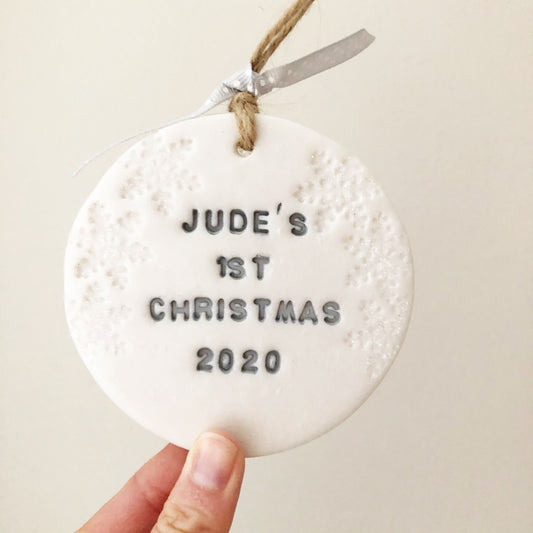 Personalised baby's 1st Christmas bauble ornament, pearlised white round clay with JUDE’S 1st CHRISTMAS 2020 in grey paint, decorated with 3 iridescent glitter snowflakes on either side of the bauble