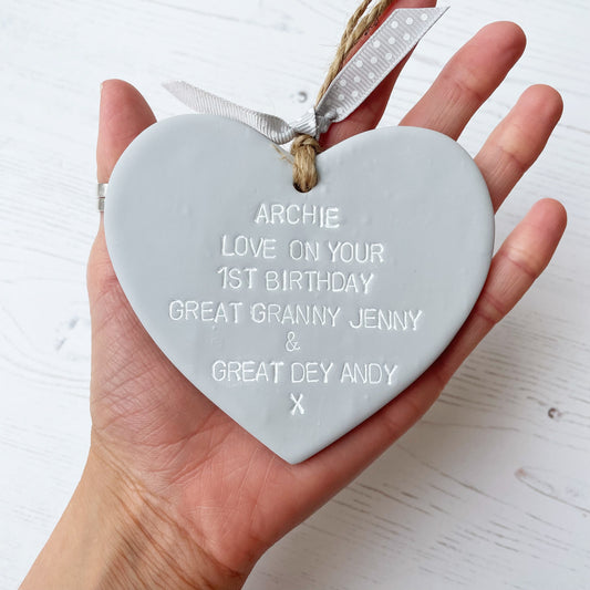 Personalised 1st birthday gift, grey clay hanging heart, the heart is personalised in white with ARCHIE LOVE ON YOUR 1ST BIRTHDAY GREAT GRANNY JENNY & GREAT DEY ANDY X