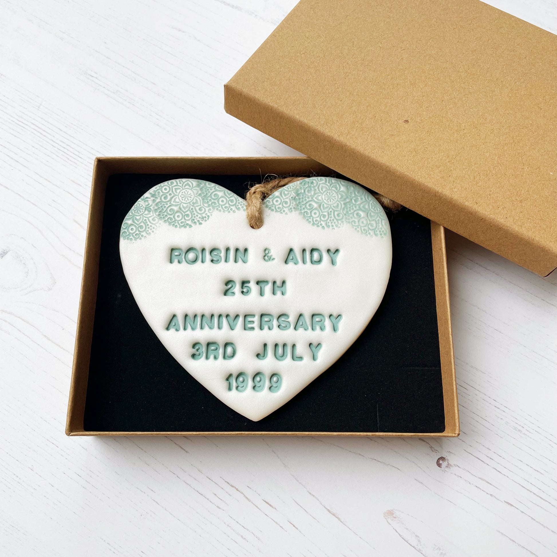 Personalised 25th anniversary gift, pearlised white clay hanging heart with a sage green lace edge at the top of the heart, the heart is personalised with ROISIN & AIDY 25TH ANNIVERSARY 3RD JULY 1999