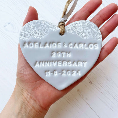 Personalised 25th anniversary gift, grey clay hanging heart with a white lace edge at the top of the heart, the heart is personalised with ADELAIDE & CARLOS 25TH ANNIVERSARY 11-8-2024