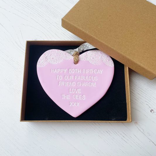 Personalised 50th birthday gift, pastel pink clay hanging heart with a white lace edge at the top of the heart, the heart is personalised with HAPPY 50TH BIRTHDAY TO OUR FABULOUS FRIEND SHARON! LOVE THE GEES XXX