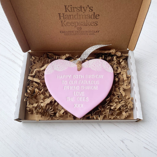 Personalised 50th birthday gift, pastel pink clay hanging heart with a white lace edge at the top of the heart, the heart is personalised with HAPPY 50TH BIRTHDAY TO OUR FABULOUS FRIEND SHARON! LOVE THE GEES XXX