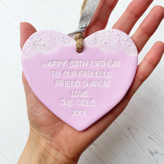 Personalised 50th birthday gift, pastel pink clay hanging heart with a white lace edge at the top of the heart, the heart is personalised with HAPPY 50TH BIRTHDAY TO OUR FABULOUS FRIEND SHARON! LOVE THE GEES XXX