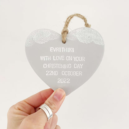 Personalised Christening baptism gift, grey clay hanging heart with a white lace edge at the top of the heart, the heart is personalised with EVRITHIKI WITH LOVE ON YOUR CHRISTENING DAY 22ND OCTOBER 2022