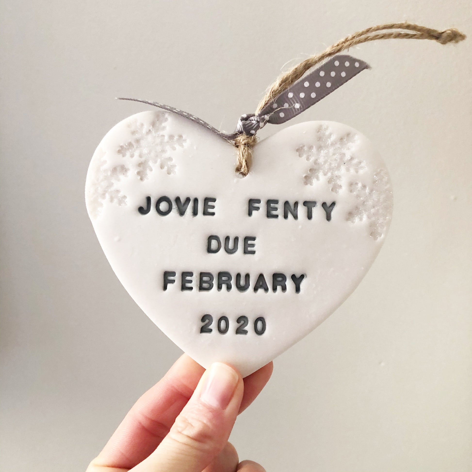 Personalised baby's first Christmas heart ornament, pearlised white clay with JOVIE FENTY DUE FEBRUARY 2020 painted grey, decorated with 2 iridescent glitter snowflakes on either side of the top of the heart