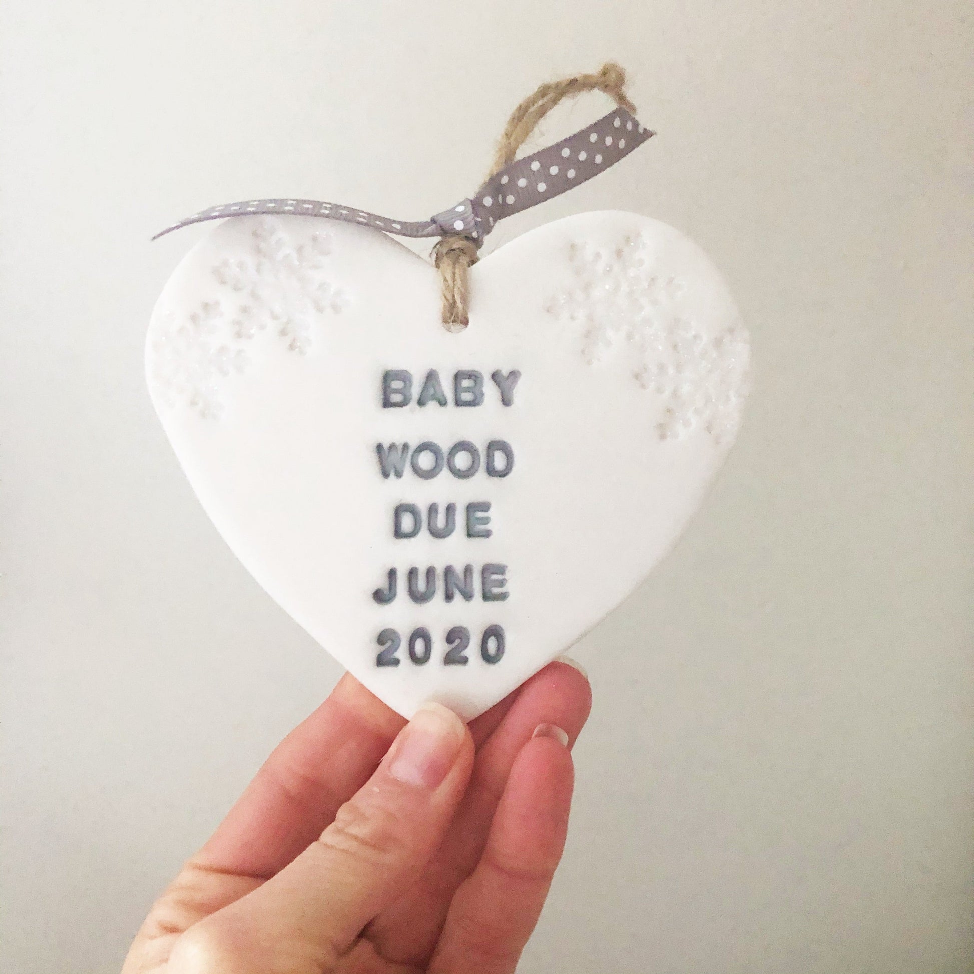 Personalised baby's first Christmas heart ornament, pearlised white clay with BABY WOOD DUE JUNE 2020 painted grey, decorated with 2 iridescent glitter snowflakes on either side of the top of the heart