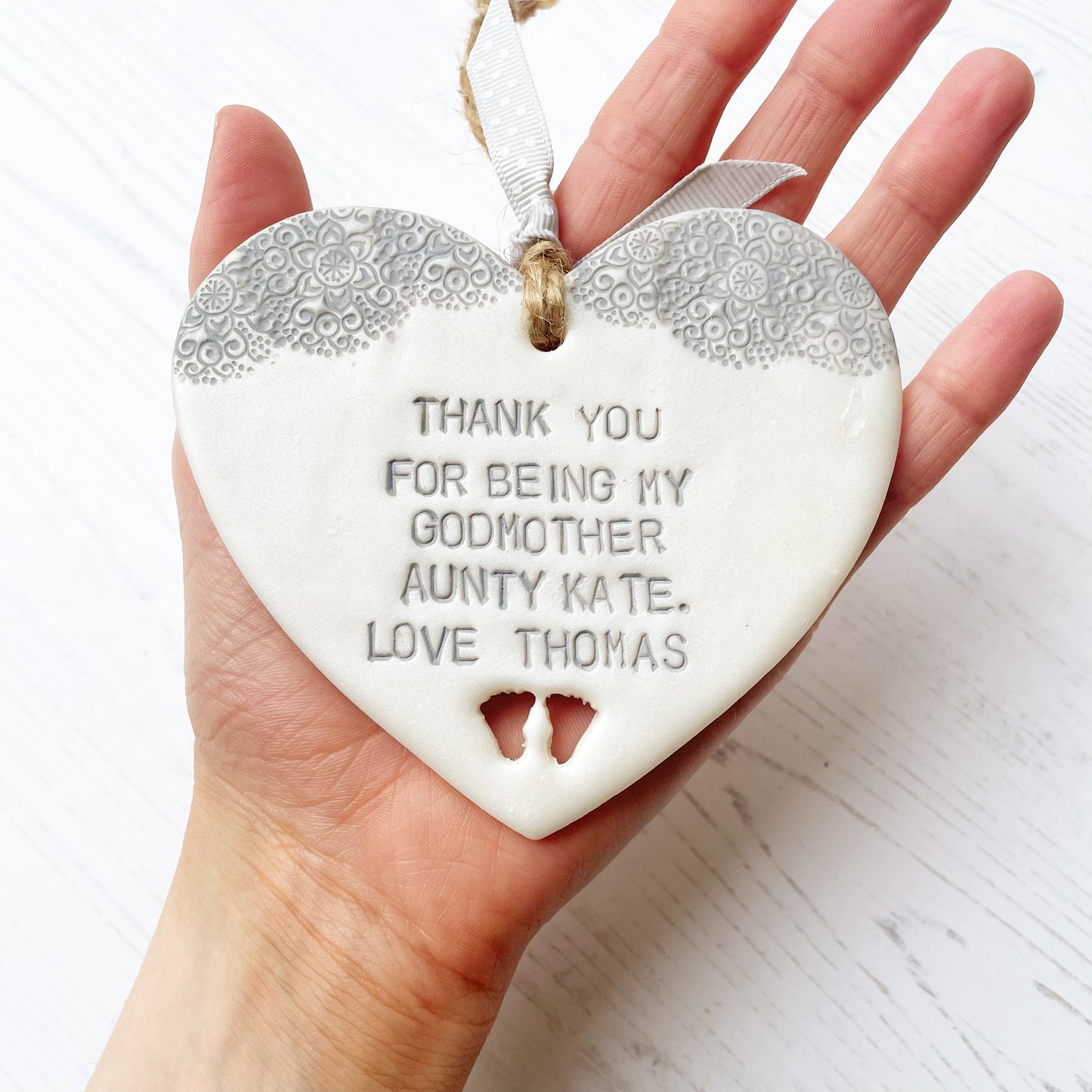 Personalised Godmother gift, pearlised white clay hanging heart with baby feet cut out of the bottom and grey lace edge at the top of the heart, the heart is personalised with THANK YOU FOR BEING MY GODMOTHER AUNTY KATE. LOVE THOMAS