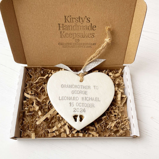 Pearlised white clay hanging heart with baby feet cut out of the bottom and grey personalisation, the heart is personalised with GRANDMOTHER TO GEORGE LEONARD MICHAEL 15TH OCTOBER 2024