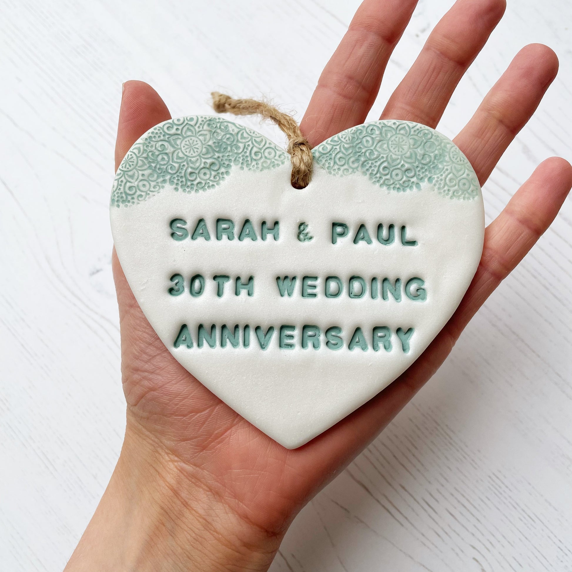 Personalised 30th anniversary gift, pearlised white clay hanging heart with a sage green lace edge at the top of the heart, the heart is personalised with SARAH & PAUL 30TH WEDDING ANNIVERSARY