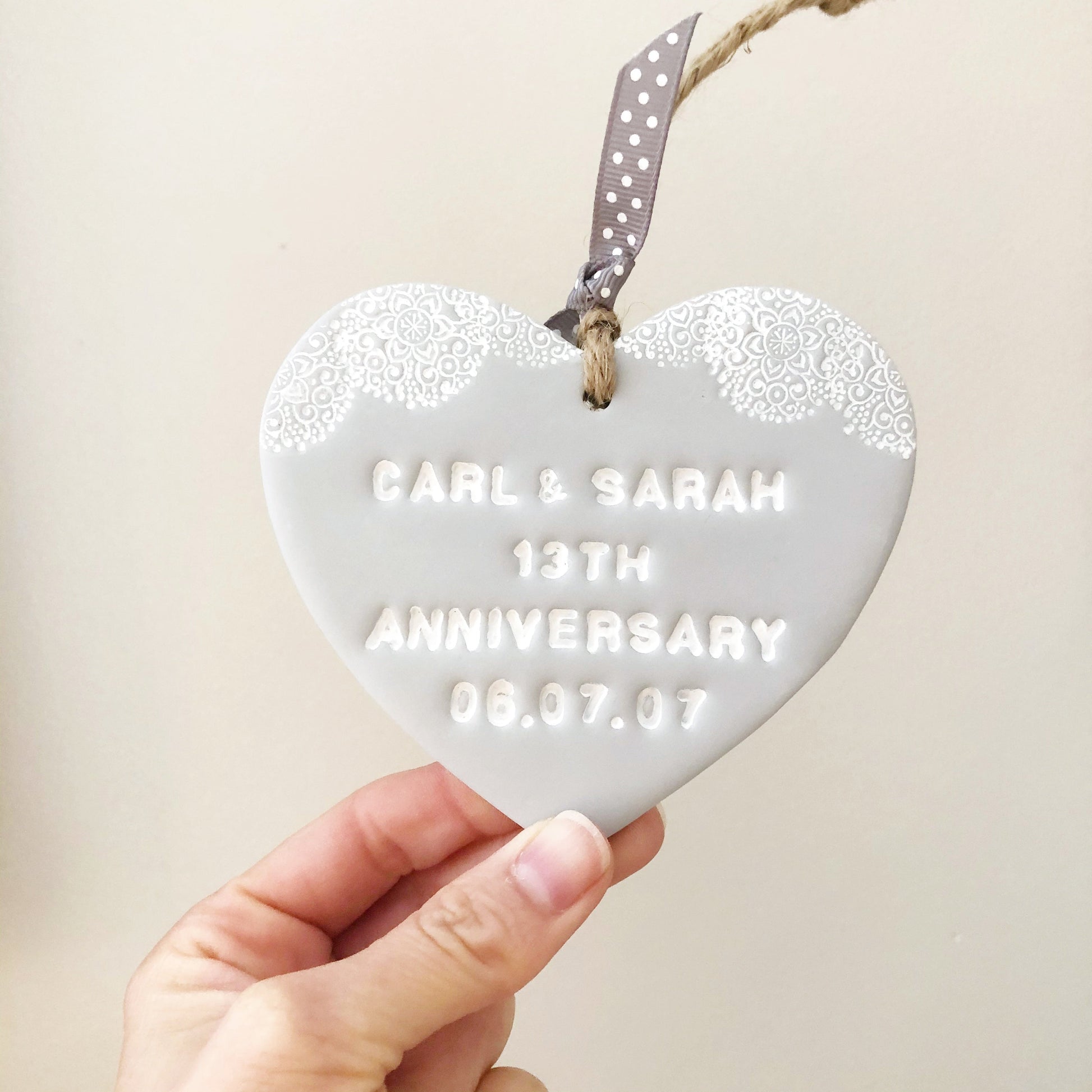 Personalised anniversary gift, grey clay heart with a white lace edge at the top of the heart with jute twine for hanging, the heart is personalised with CARL & SARAH 13TH ANNIVERSARY 06.07.07