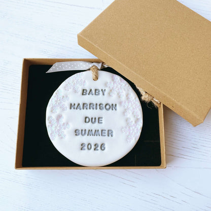 Personalised baby due Christmas bauble ornament, pearlised white round clay with BABY HARRISON DUE SUMMER 2026 in grey paint, decorated with 3 iridescent glitter snowflakes on either side of the bauble