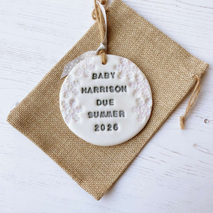 Personalised baby due Christmas bauble ornament, pearlised white round clay with BABY HARRISON DUE SUMMER 2026 in grey paint, decorated with 3 iridescent glitter snowflakes on either side of the bauble