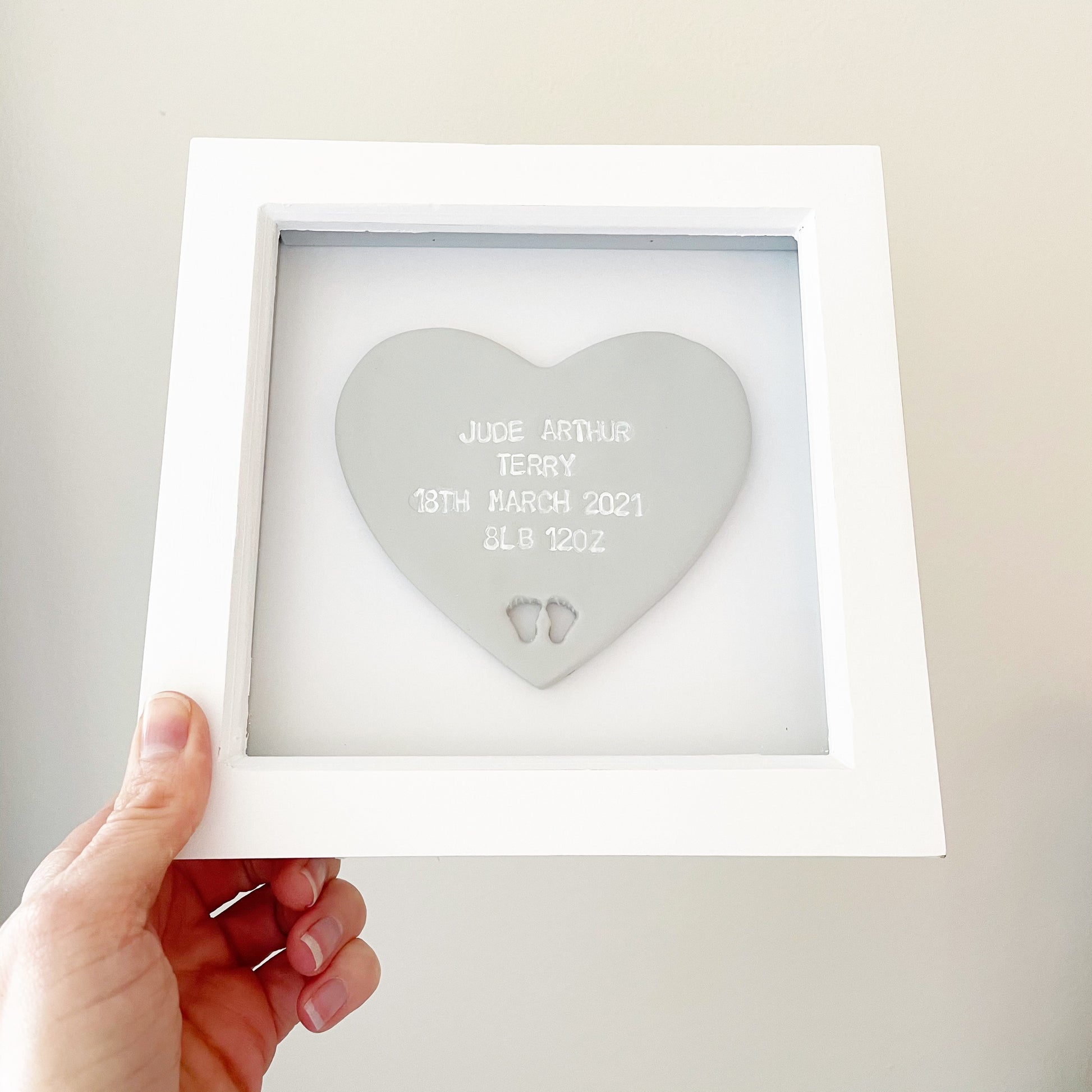 Personalised baby keepsake gift, grey clay heart with baby feet cut out at the bottom of the heart in a white box frame, the heart is personalised with the baby’s name, date of birth, weight and time