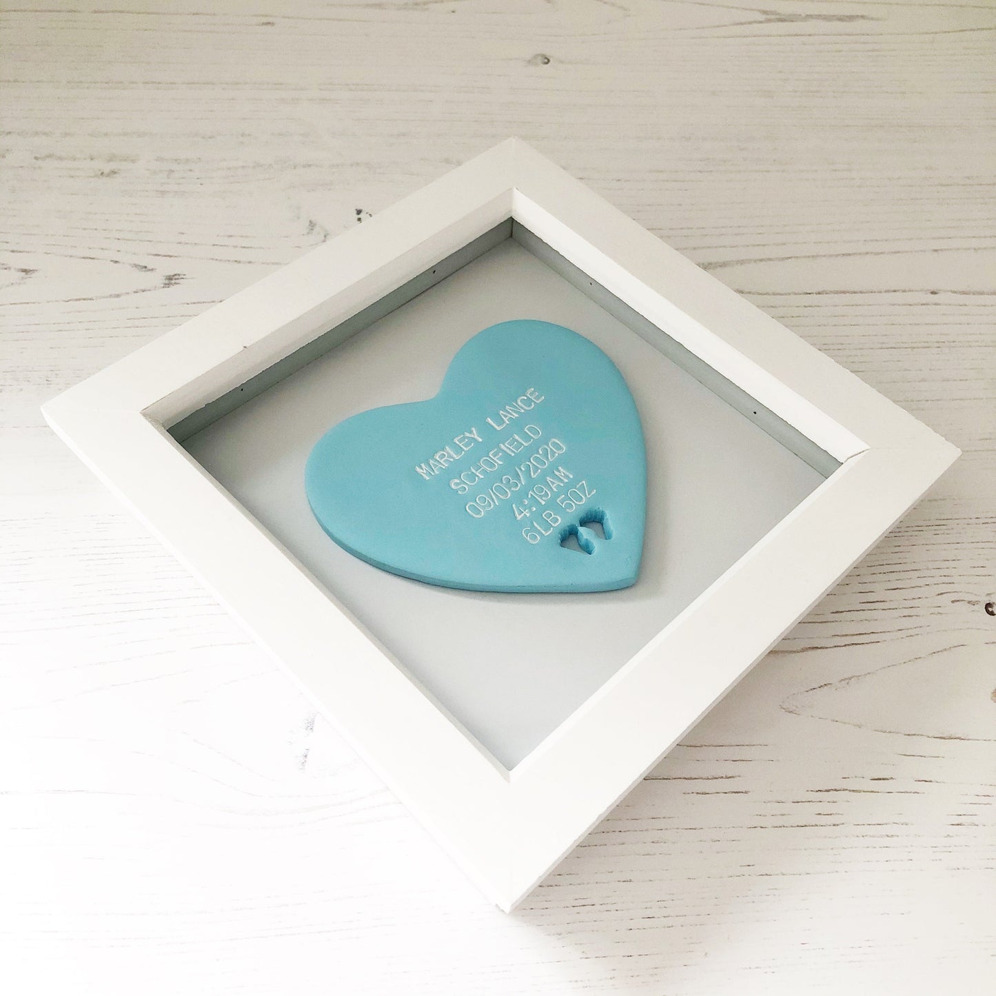 Personalised baby keepsake gift, pastel blue clay heart with baby feet cut out at the bottom of the heart in a white box frame, the heart is personalised with the baby’s name, date of birth, weight and time