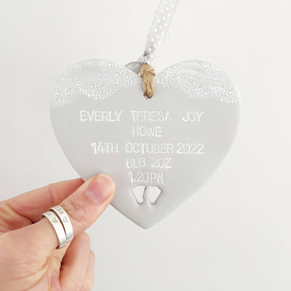 Personalised baby keepsake gift, grey clay hanging heart with baby feet cut out at the bottom of the heart and white lace edge to the top, the heart is personalised with the baby’s name, date of birth, weight and time