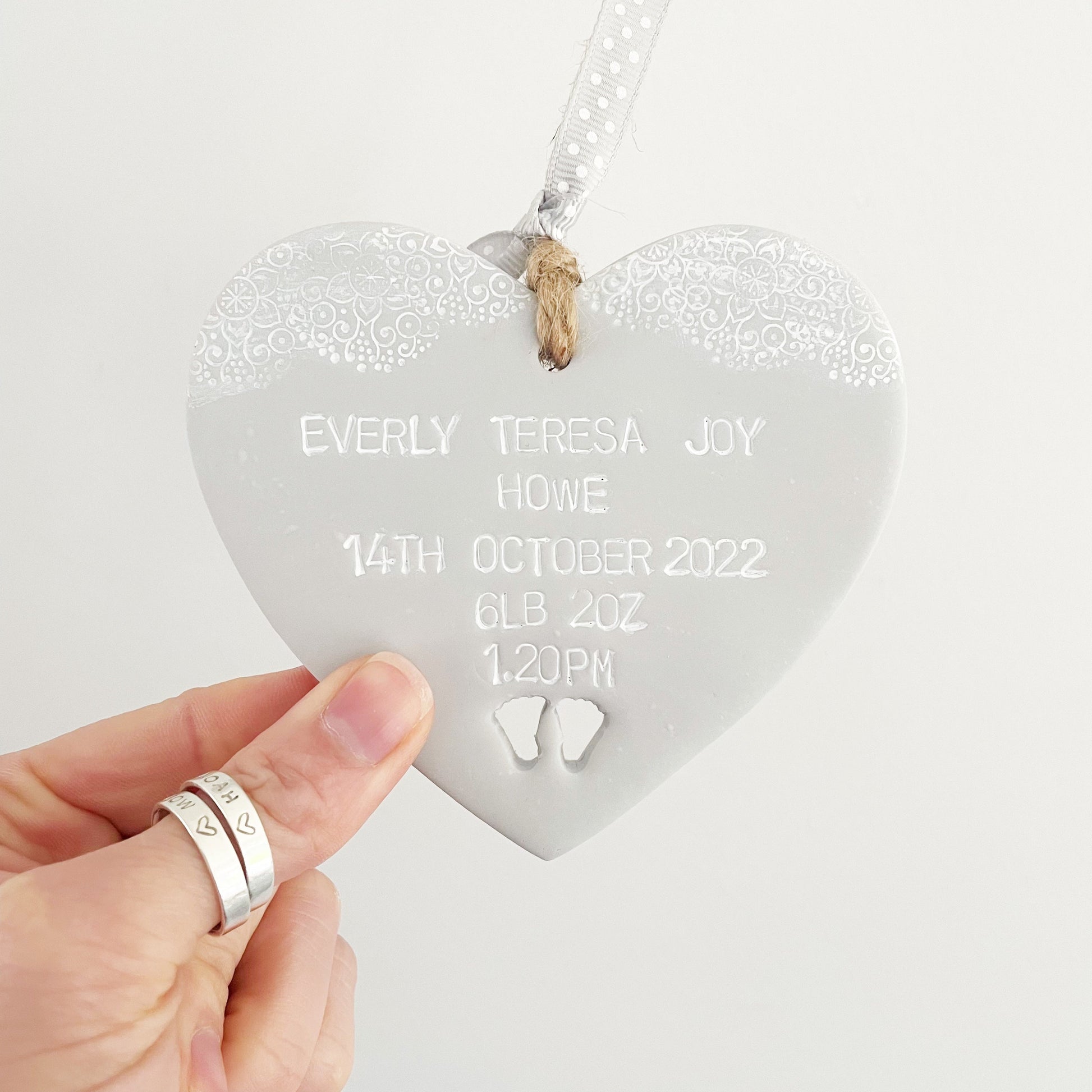 Personalised baby keepsake gift, grey clay hanging heart with baby feet cut out at the bottom of the heart and white lace edge to the top, the heart is personalised with the baby’s name, date of birth, weight and time