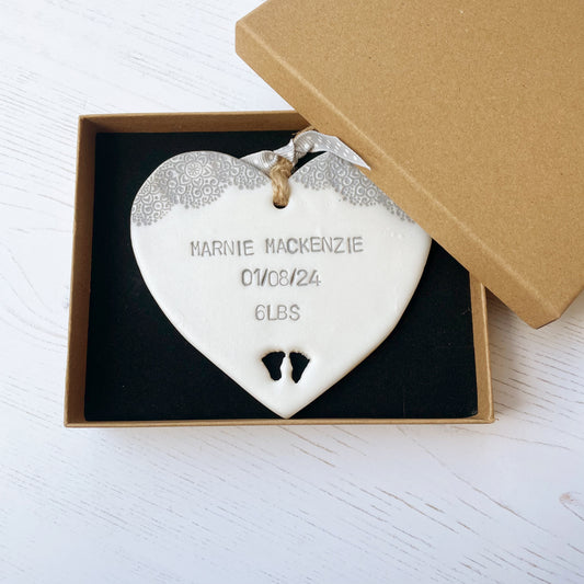 Personalised baby keepsake gift, pearlised white clay hanging heart with a grey lace edge top and baby feet cut out at the bottom of the heart, the heart is personalised with the baby’s name, date of birth and weight