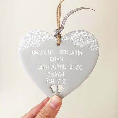 Personalised baby keepsake gift, grey clay hanging heart with baby feet cut out at the bottom of the heart and white lace edge to the top, the heart is personalised with the baby’s name, date of birth, weight and time