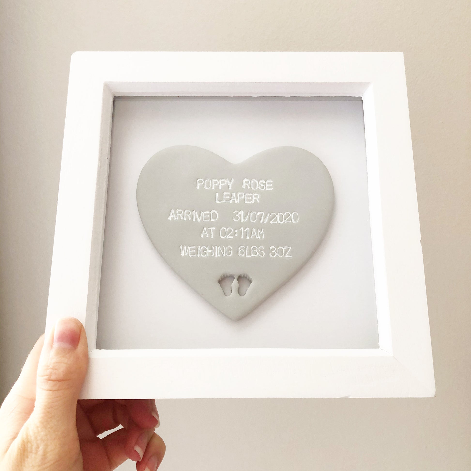 Personalised baby keepsake gift, grey clay heart with baby feet cut out at the bottom of the heart in a white box frame, the heart is personalised with the baby’s name, date of birth, weight and time