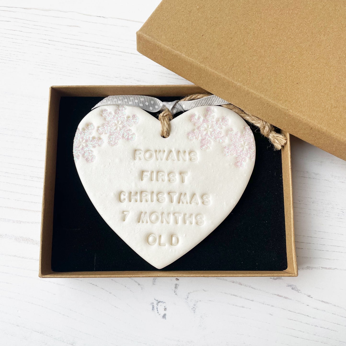 Personalised baby’s first Christmas heart ornament, pearlised white clay with ROWANS FIRST CHRISTMAS 7 MONTHS OLD (text not painted), decorated with 2 iridescent glitter snowflakes on either side of the top of the heart