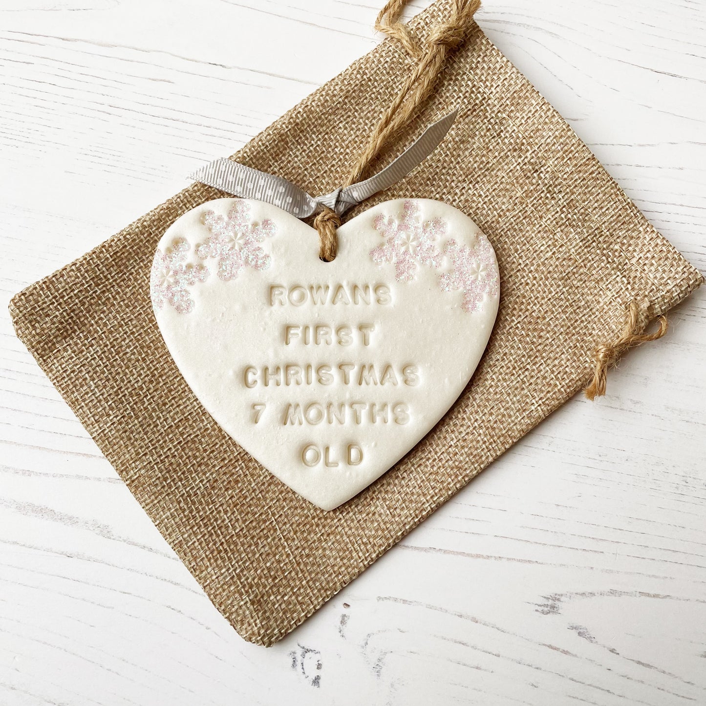 Personalised baby’s first Christmas heart ornament, pearlised white clay with ROWANS FIRST CHRISTMAS 7 MONTHS OLD (text not painted), decorated with 2 iridescent glitter snowflakes on either side of the top of the heart