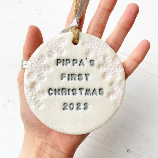 Personalised baby's first Christmas bauble ornament, pearlised white round clay with PIPPA’S FIRST CHRISTMAS 2023 in grey paint, decorated with 3 iridescent glitter snowflakes on either side of the bauble