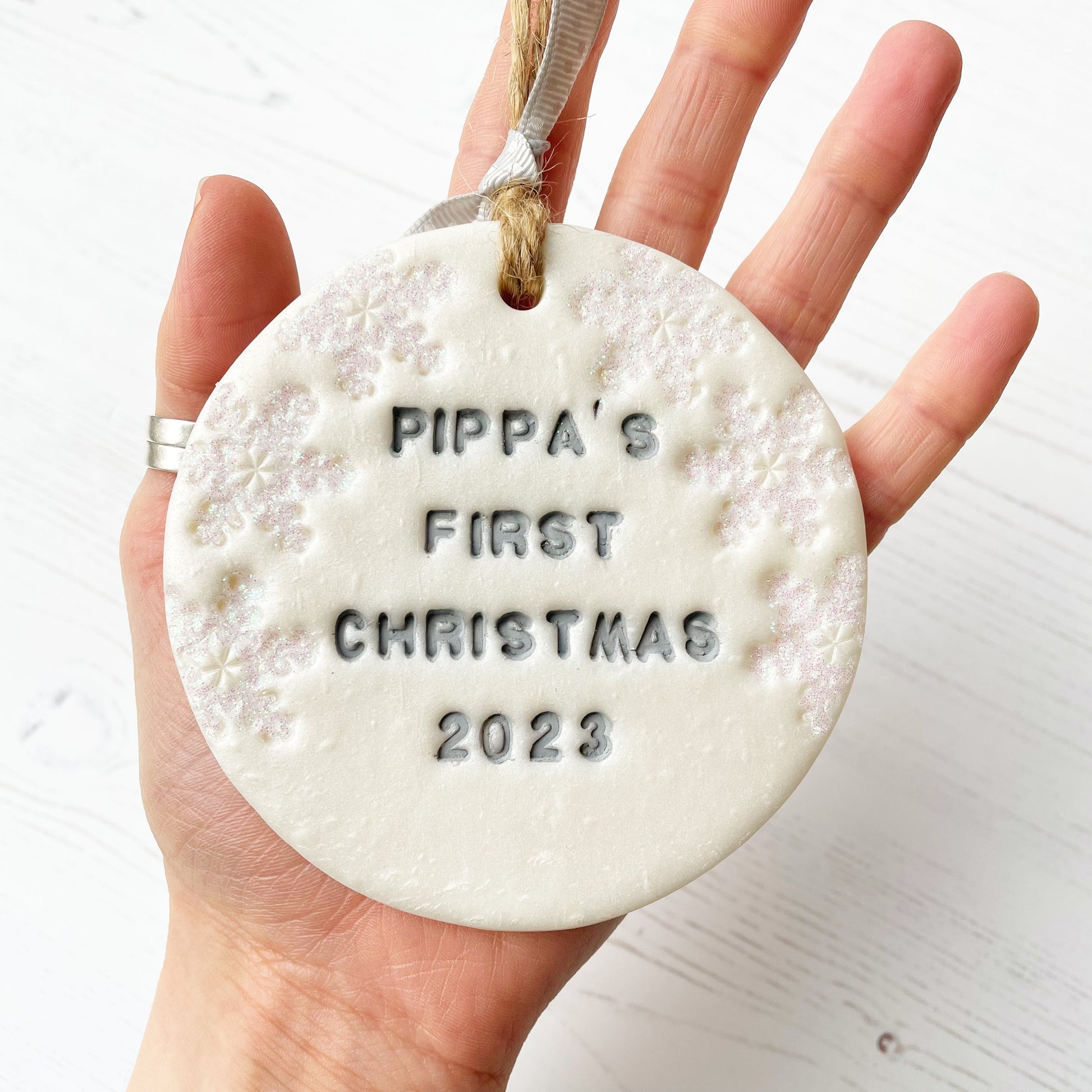 Personalised baby's first Christmas bauble ornament, pearlised white round clay with PIPPA’S FIRST CHRISTMAS 2023 in grey paint, decorated with 3 iridescent glitter snowflakes on either side of the bauble