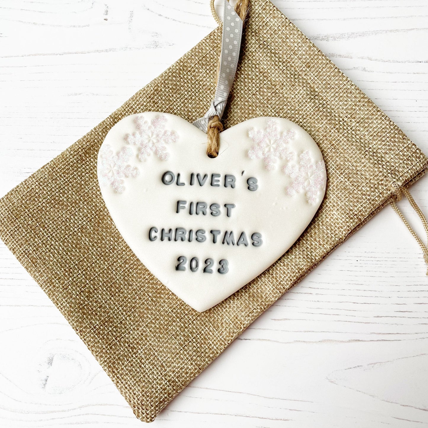 Personalised baby's first Christmas heart ornament, pearlised white clay with OLIVER'S FIRST CHRISTMAS 2023 painted grey, decorated with 2 iridescent glitter snowflakes on either side of the top of the heart